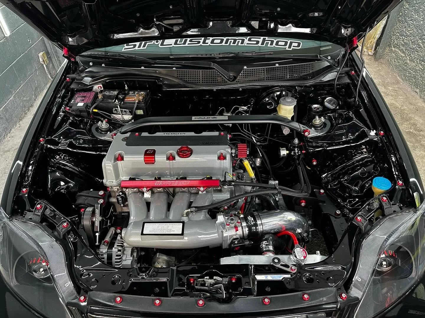 Bahía de motor Honda con acabados negros, componentes pulidos y tornillería roja de Sir Custom Shop